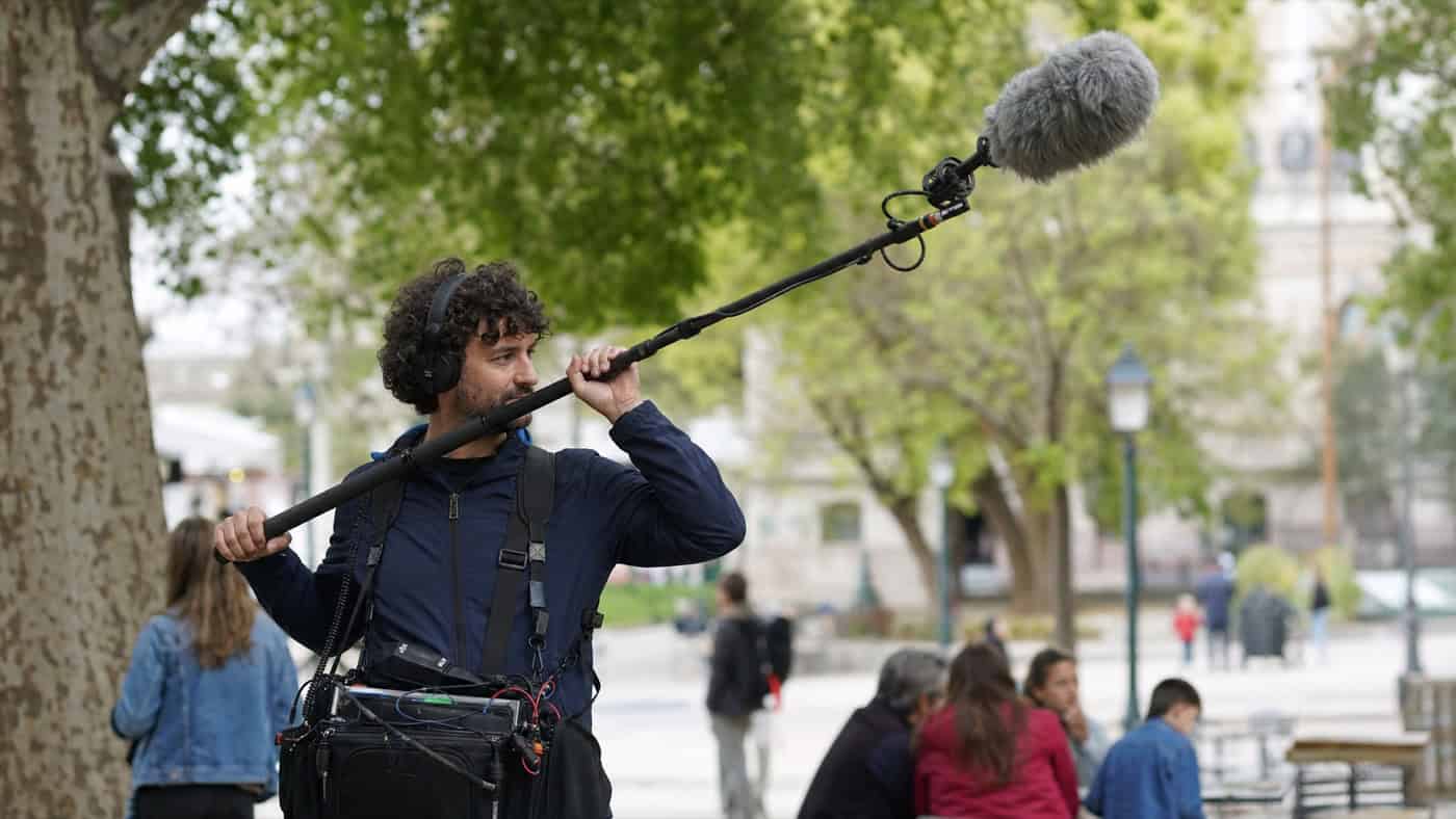 Ingénieur du son en extérieur avec un microphone directionnel sur une perche, enregistrant les sons ambiants à la lumière naturelle.
