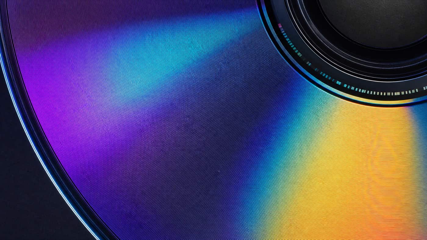폴리카보네이트 재질의 데이터 나선 부분에 무지개 빛깔의 반사가 나타나는 CD 표면의 접사 이미지.